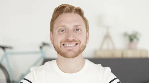 Cheerful red haired young man smiling at camera on video call from home Stock Footage 174310261