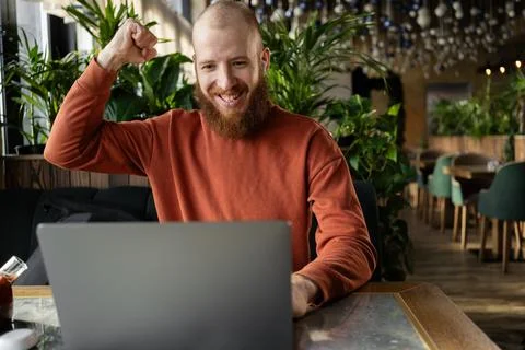 Cheerful redhead man millennial with beard talking online on laptop in cafe,  Stock Photos