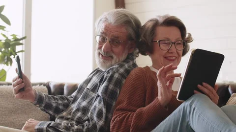 Cheerful retired couple using smartphone and digital tablet. Smiling senior Stock Footage 242611391