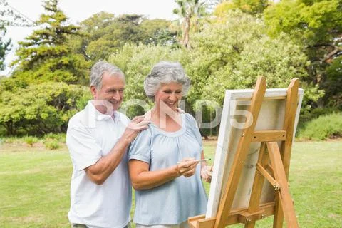 Cheerful retired woman painting on canvas with husband Stock Photos