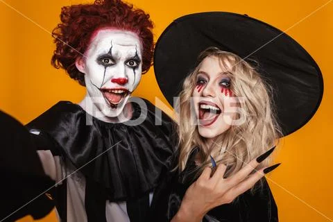 Cheerful scary witch and clown making selfie isolated Stock Photos