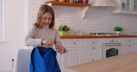 Cheerful school kid packing backpack and getting ready for exciting day of Stock Footage 332997775