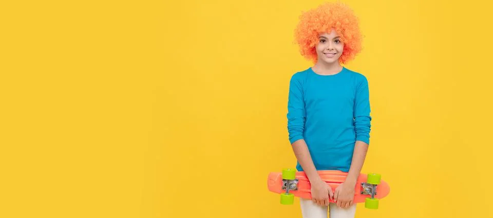 Cheerful selfish child girl in curly wig hold penny board, copy space, childhood Stock Photos
