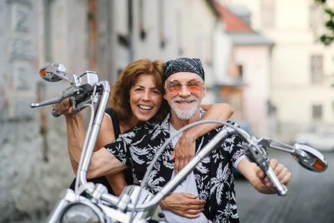 A cheerful senior couple travellers with motorbike in town. Stock Photos