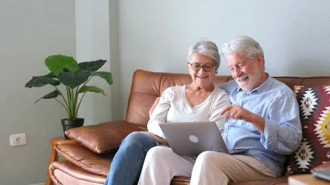 Cheerful senior couple using laptop while sitting on sofa and smiling. Elderly h Stock Footage 166244550