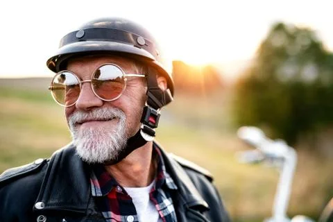 A cheerful senior man traveller with motorbike in countryside, headshot. Stock Photos