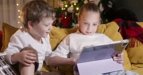 Cheerful siblings sit on couch and play engaging game on tablet Vidéo 316752689