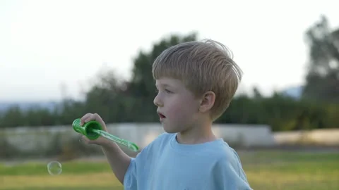Cheerful small child blows bubbles closeup in a park setting. Fun summer Stock Footage 317316896