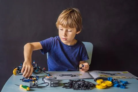 Cheerful smart schoolboy sitting at the table and constructing a robotic device 写真素材
