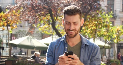 Cheerful Smiling Man is Browsing his Cellphone for Work in Sunny City Center.  Stock Footage 99235086