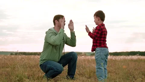Cheerful son gives high-five to father in field with landscape view of nature Stock Footage 254461542