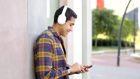 Cheerful student using phone leaning on a wall in the campus Stock Footage 258326285