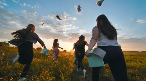 Cheerful students run throwing notebooks after school at sunset. Stock Photos