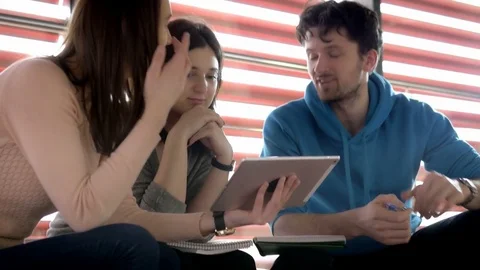 Cheerful students talking while holding a tablet in the library Video stock 75555115