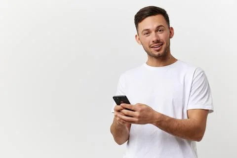 Cheerful tanned handsome man in basic t-shirt typing message with phone smile at Foto stock