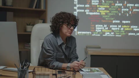 Cheerful Teacher Sitting at Desk Explaining Code on Projection Stock Footage 244700405