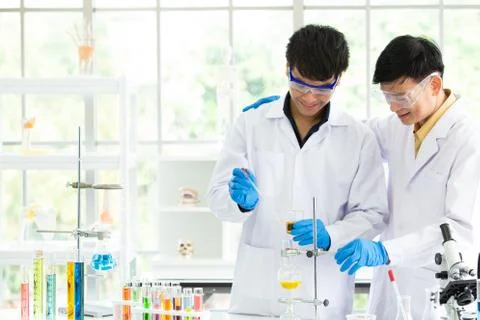 Cheerful Team of microbiologists wearing safety goggles looking at test tube. Stock Photos