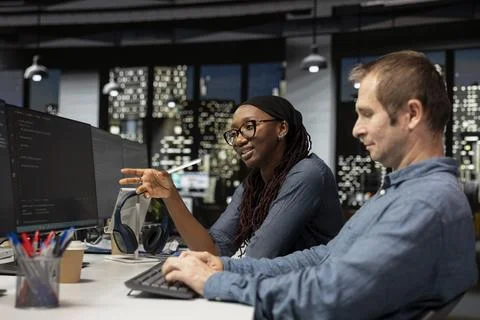 Cheerful tech startup intern asks questions to senior programmer Stock Photos