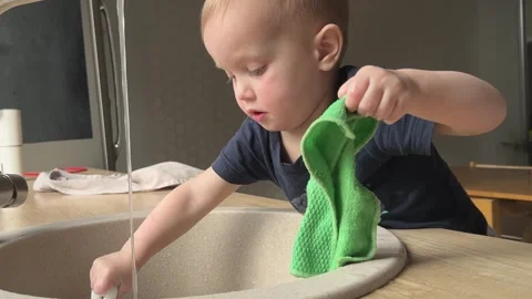 A cheerful toddler joyfully playing with water in a modern kitchen sink Stock Footage 312440468