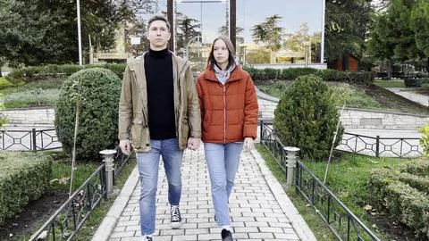Cheerful two young spouses strolling on street in autumn park happy lovely co Stock Photos