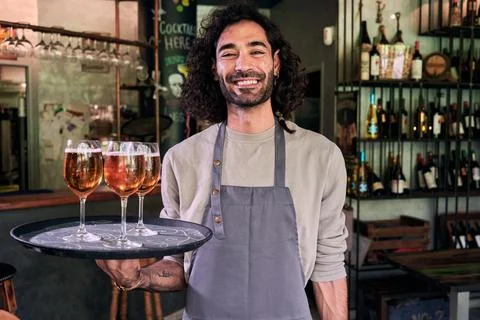 Cheerful waiter looking at camera while holding a tray with beers at place of Stock Photos