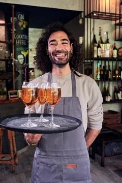 Cheerful waiter looking at camera while holding a tray with beers at place of Stock Photos
