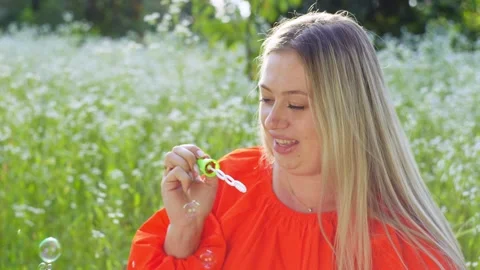 A cheerful woman blows soap bubbles in the midst of a field of chamomiles. Stock Footage 254468053