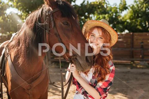 Cheerful woman cowgirl in hat with her horse in village Stock Photos
