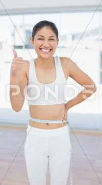 Cheerful woman measuring waist while gesturing thumbs up Stock Photos