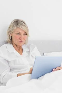 Cheerful woman sitting in bed using tablet pc 스톡 사진