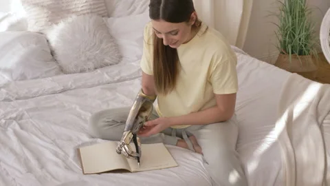 Cheerful woman writes in notebook with bionic arm on bed Stock Footage 150222965