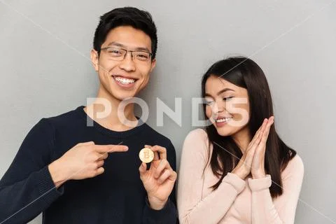 Cheerful young asian loving couple holding bitcoin. Stock Photos