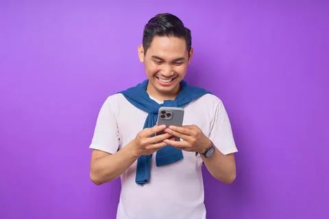 Cheerful young Asian man using smartphone for messaging with friends isolat.. Stock Photos