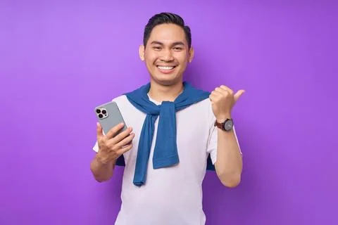 Cheerful young Asian man using mobile phone and showing thumb up gesture is.. Stock Photos
