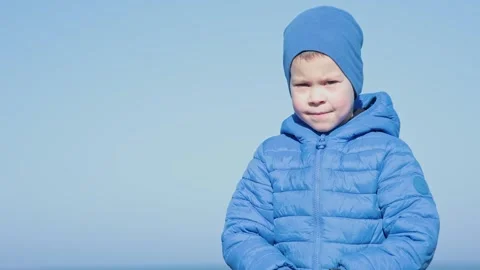 A Cheerful Young Boy Dressed in a Blue Winter Attire Against a Bright Clear Sky Stock Footage 304729577