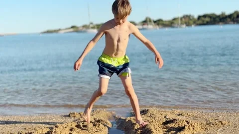 Cheerful young boy playing in the sand at the seashore, digging a trench with 스톡 동영상 332253858