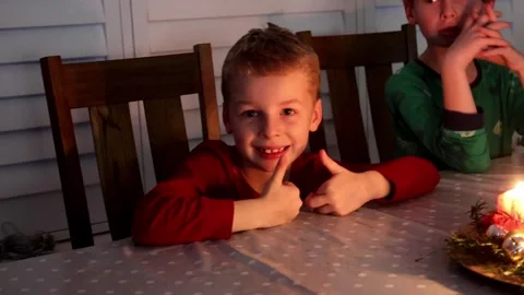A cheerful young boy sits at a dining table indoors, smiling directly at the Stock Footage 332410857
