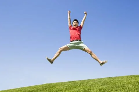  Cheerful young Chinese man jumping on grass Beijing China Copyright: xLia... Stock Photos