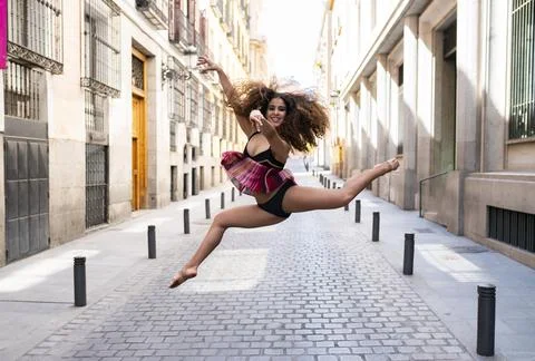 Cheerful young ethnic ballerina jumping on street Stock Photos