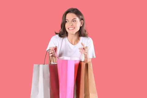 Cheerful young girl in basic clothes using mobile phone while holding shoppin Stock Photos