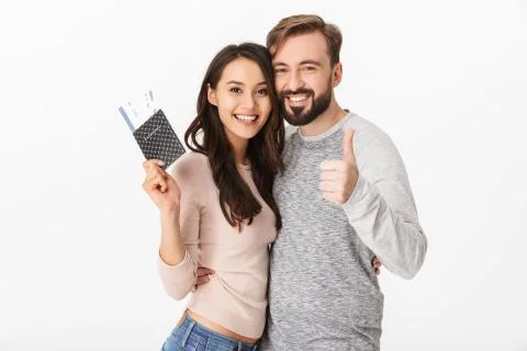 Cheerful young loving couple holding passport and tickets showing thumbs up. Stock Photos