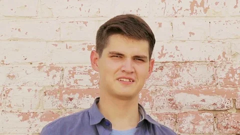 Cheerful young man close-up in a blue shirt. At the white brick wall Stock Footage 79362897