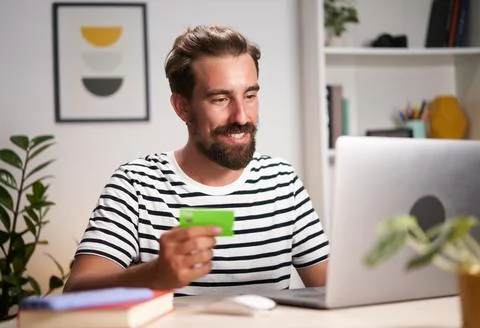 Cheerful young man doing e-shopping at home. Happy caucasian male making online Stock Photos
