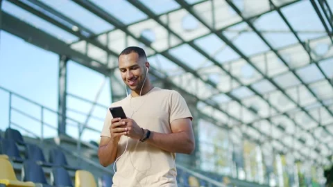 A cheerful young man with earphones using his smartphone while walking Stock Footage 280688333