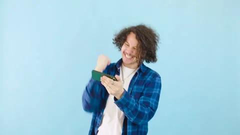 Cheerful young man having a great time enjoying mobile games on a bright blue Stock Footage 281048757