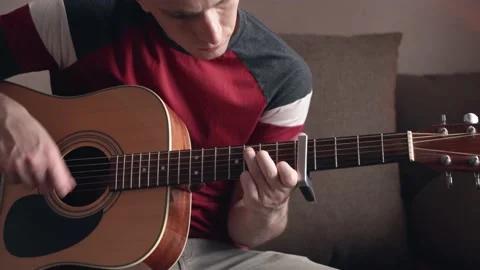 Cheerful young man is learning to play the acoustic guitar. Видео 208882008