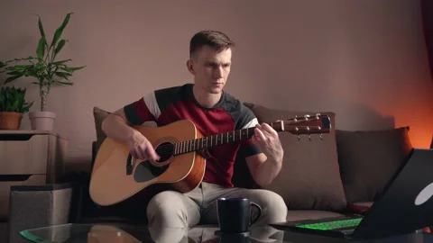 Cheerful young man is learning to play the acoustic guitar. 库存影片 208882160