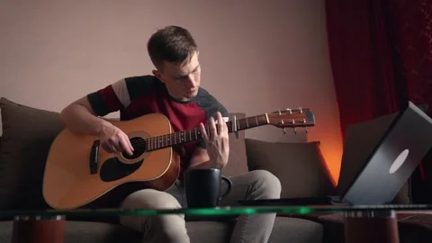 Cheerful young man is learning to play the acoustic guitar. Stock Footage 209308640