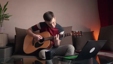 Cheerful young man is learning to play the acoustic guitar. Stock Footage 211813268