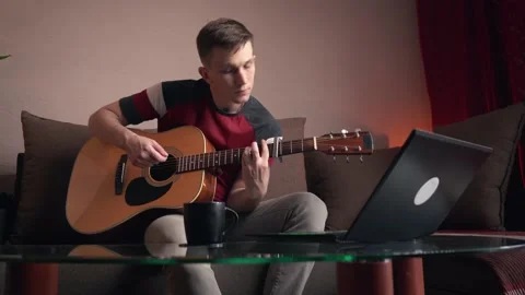 Cheerful young man is learning to play the acoustic guitar. remote online Stock Footage 212613540
